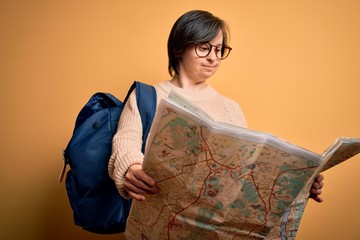 Canvas Print - Young down syndrome tourist woman wearing bag and looking at destination city map with a happy face standing and smiling with a confident smile showing teeth