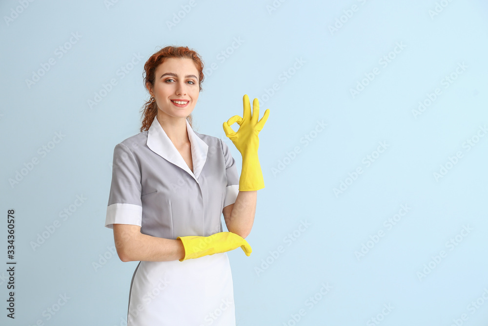 Beautiful young chambermaid showing OK on color background