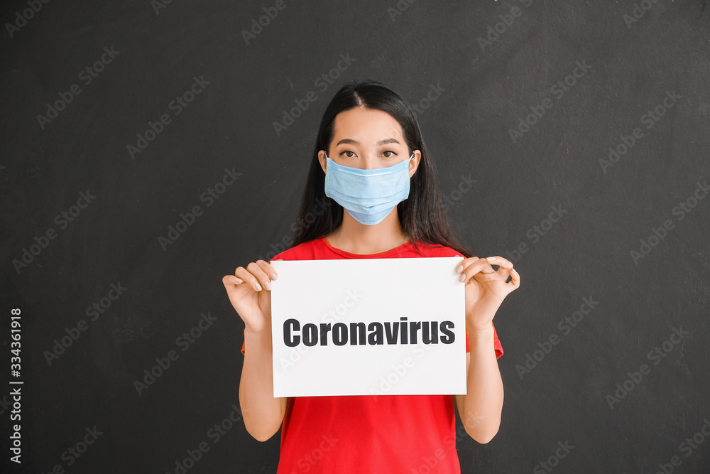 Asian woman holding paper sheet with text CORONAVIRUS on dark background