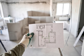 The construction worker hold in hands Architectural blueprints. Repair or construction of a new apartment. Concept for new house design or home improvement. Development of the apartment project.