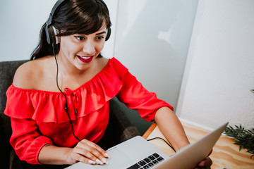 young latin woman sitting alone home office working on a laptop and listening to music on earphones, Mexican girl in Mexico working at home