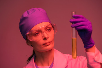 Poster - Young female laboratory worker looking at yellow liquid substance in flask