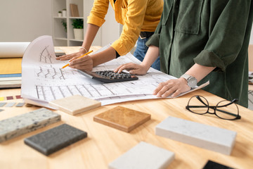 Poster - Young female architect pointing at blueprint and explaining sketch to colleague
