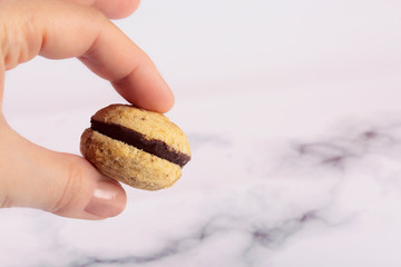 Female hand holds a cookie called Bacio di dama on a marble background