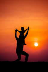 silhouette of a family with a boy riding his father's neck happily against the sunset sky