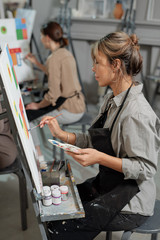 Poster - One of young students of painting course sitting in front of easel