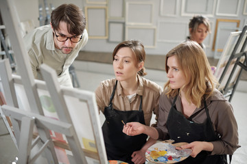 Poster - Two girls in aprons showing painting on easel to their teacher at lesson