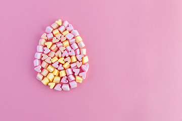 Easter egg shape from multi-colored little marshmallows hearts on a pink background. Concept. Copy space