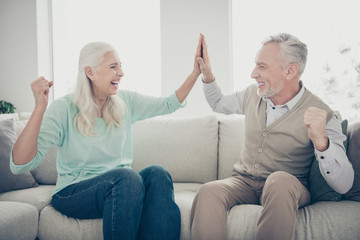Wall Mural - Portrait of lovely grandparents give high-five celebrate dressed teal brown pullover jeans trousers sit cozy divan scream shout in apartment indoors