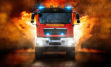 Fototapeta Sport - Feuerwehrfahrzeug mit Blaulicht und mit Flammen im Hintergrund