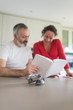 © Rafa Fernandez - Happy pregnant woman with her husband sitting at home. Smiling couple consulting a book at the kitchen.