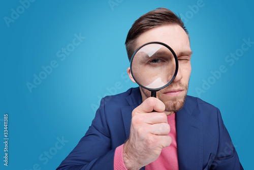 Fotomural Serious young male detective holding magnifying glass by right eye