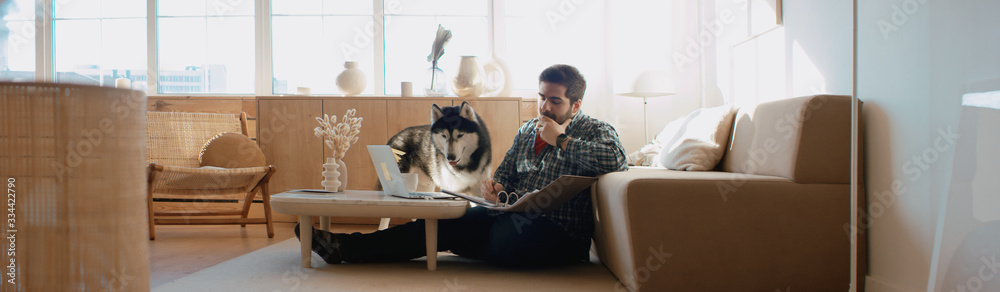 Middle Eastern male working from home, having a video call, dog sits near him. Stay home, quarantine remote work - obrazy, fototapety, plakaty 