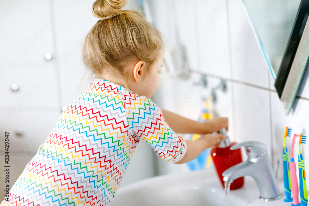 Cute little toddler girl washing hands with soap and water in bathroom. Adorable child learning cleaning body parts. Hygiene routine action during viral desease. kid at home or nursery. - obrazy, fototapety, plakaty 