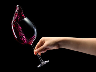 Woman hand holding red wine glass with splashes isolated on black.