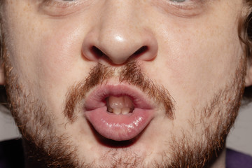 Whispering. Close up of face of beautiful caucasian young man with redhair beard, focus on mouth. Human emotions, facial expression, cosmetology, body and skin care concept. Well kept skin. Wellbeing.