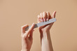 © LIGHTFIELD STUDIOS - Partial view of woman filing fingernails with emery board isolated on beige