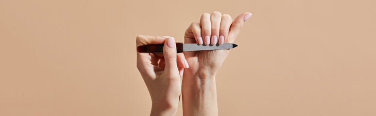 Wall Mural - Cropped view of woman filing nails isolated on beige, panoramic shot