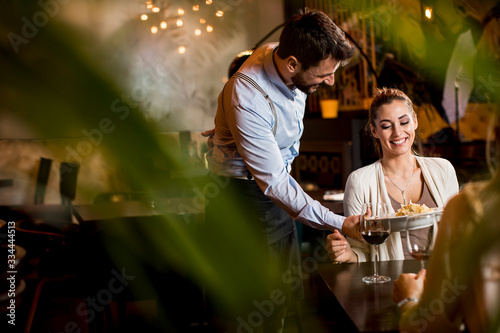 Fotografía Smiling young female friends at a restaurant with waiter serving dinner