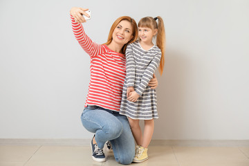 Poster - Woman and her little daughter taking selfie near light wall