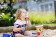 © Irina Schmidt - Beautiful little blonde toddler girl having fun with blowing soap bubble blower. Cute adorable baby child playing on playground on sunny summer day. Happy active funny healthy kid