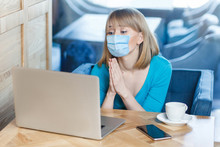Please Help. Portrait Of Worry Young Woman With Surgical Medical Mask Is Sitting And Working On Laptop And Looking Display And Begging On Video Call. Indoor Working, Medicine And Health Care Concept.