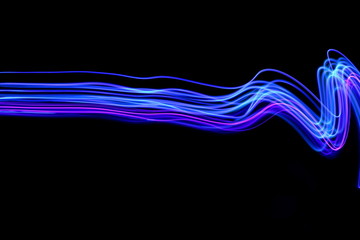 Wall Mural - Long exposure photograph of neon blue and purple streaks of light in an abstract swirl, parallel lines pattern against a black background. Light painting photography.