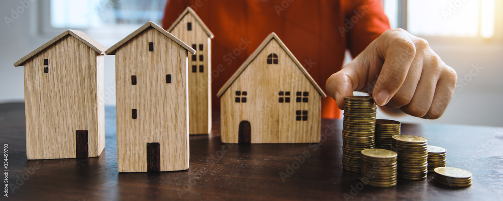 Save to real estate, property owner get money to home concept, small wooden house model on table with hand stacked coins to rent or buy above mentioned residence with cash to bank agency - obrazy, fototapety, plakaty 