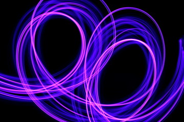 Wall Mural - Long exposure photograph of neon purple streaks of light in an abstract swirl, parallel lines pattern against a black background. Light painting photography.