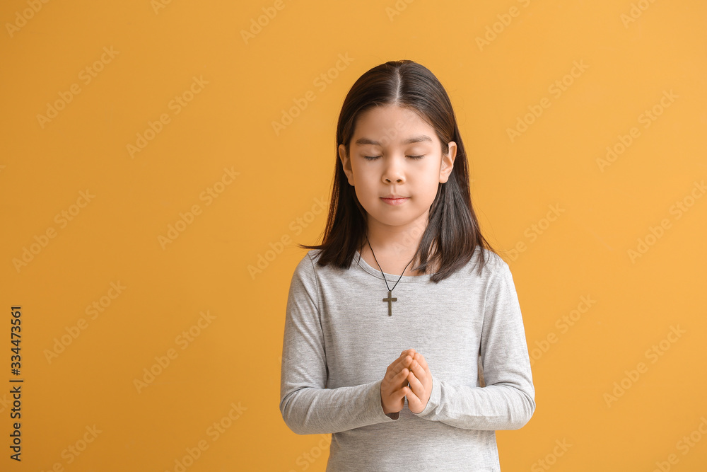 Cute little Asian girl praying on color background