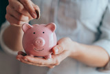 Fototapeta  - female hands hold a pink piggy bank and puts a coin there. The concept of saving money or savings, investment