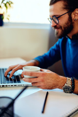 Wall Mural - Young handsome bearded hipster sitting at his home office looking at his notebook. Work from home concept.