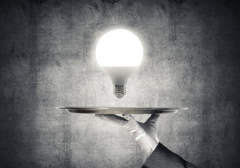 Wall Mural - Hand of waitress presenting lightbulb on tray.