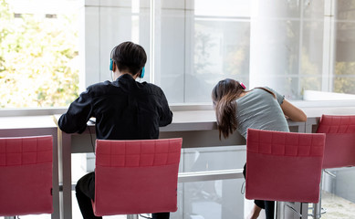 Back side of young teenagers wearing headphone on hea,sitting beside window