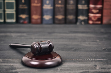 Wall Mural -  Judge Gavel on a black wooden background in front of a law library.