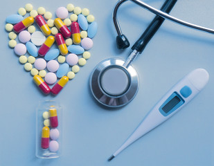 Stethoscope, thermometer and pills like a heart on a blue background