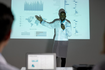 Poster - Confident young Afro-American medical scientist in lab coat showing statistics on spread of coronavirus while presenting solution to stop it