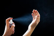 © Olena Bloshchynska - Man hands using sanitizer spray for hand hygiene on black background.