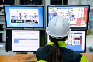 Inside the large Industry Factory Female Computer Engineer Works on Personal Computer She coding program for control machine,Thailand people work on fours monitors,Programmer working with serious