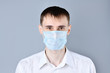 © borislav15 - Man in a medical mask. A handsome dark-haired, brown-eyed man in a white shirt and medical mask  ,dressing gown looking at camera , on a gray background. Chinese Coronavirus , Covid-19