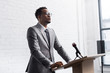 © LIGHTFIELD STUDIOS - confident african american business speaker standing on podium with microphone in conference hall