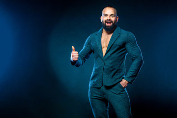 Wall Mural - Portrait of handsome stylish man bodybuilder with naked torso in elegant suit. Guy showing thumbs up sign with fingers.