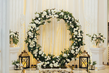 Wedding arch at the restaurant. Round flower arch. Trend in the wedding banquet room is a white  arch decorated with flowers and greens, in the background white cloth.