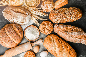 Wall Mural - Fresh bakery food, rustic crusty loaves of bread and buns on black stone background. Top view and copy space for text.