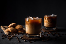A Horizontal Photo Of 2 Rocks Glasses With Cold Iced Coffee With Milk, Coffee Beans Around, Cookies, Dark Background, Deep Shadows