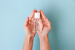 Cropped shot of female hands with antibacterial liquid bottle. Woman holding translucent sanitizer gel over blue background with a lot of copy space for text. Close up, top view, pov.