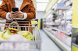 © Sam Edwards/Caia Image - Woman with smart phone pushing shopping cart in supermarket