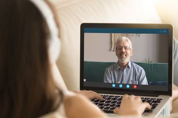 Wall Mural - Back view of young girl relax on couch speak on video call on laptop with elderly father, millennial female communicate online use Webcam conference application talk with senior dad from home