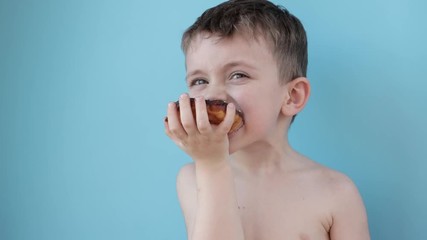 Wall Mural - Little boy eating donut chocolate on blue background. Cute happy boy smeared with chocolate around his mouth. Child concept, tasty food for kids