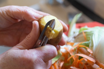 Wall Mural - To peel a potato with a peeler in a kitchen